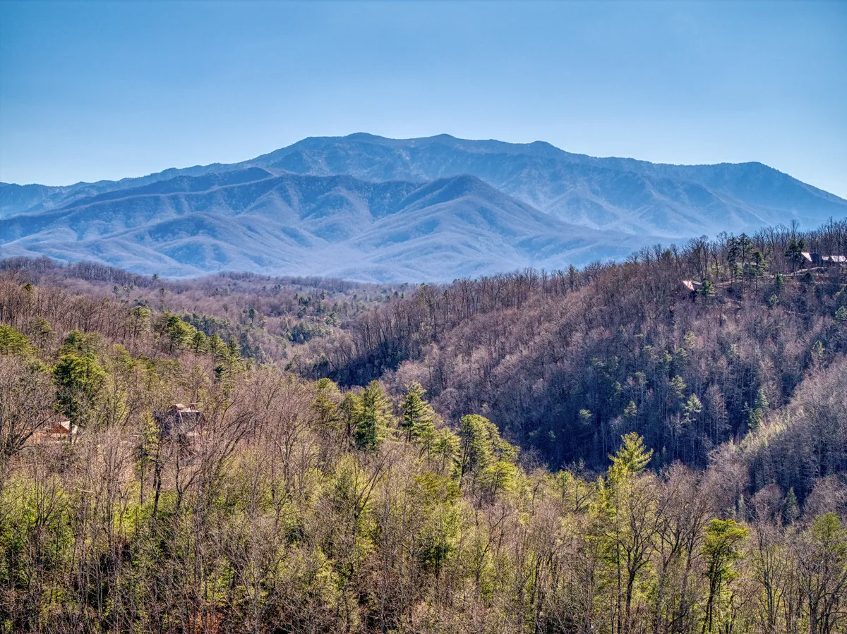 A panoramic view of the Smoky Mountains at sunrise, with lush valleys below and scattered cabins nestled in the landscape. The tranquil scene hints at opportunities for hiking, wildlife spotting, and photography.