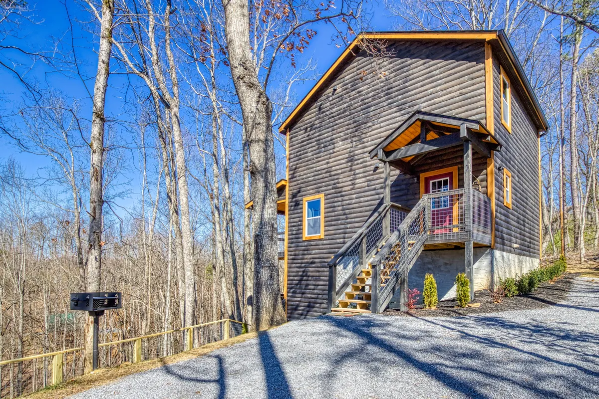 A wooden cabin set amidst natural greenery, with a staircase and nearby mailbox suggesting access and welcome. The cabin’s porch hints at opportunities for stargazing or enjoying morning coffee, and the surrounding landscape invites exploration.