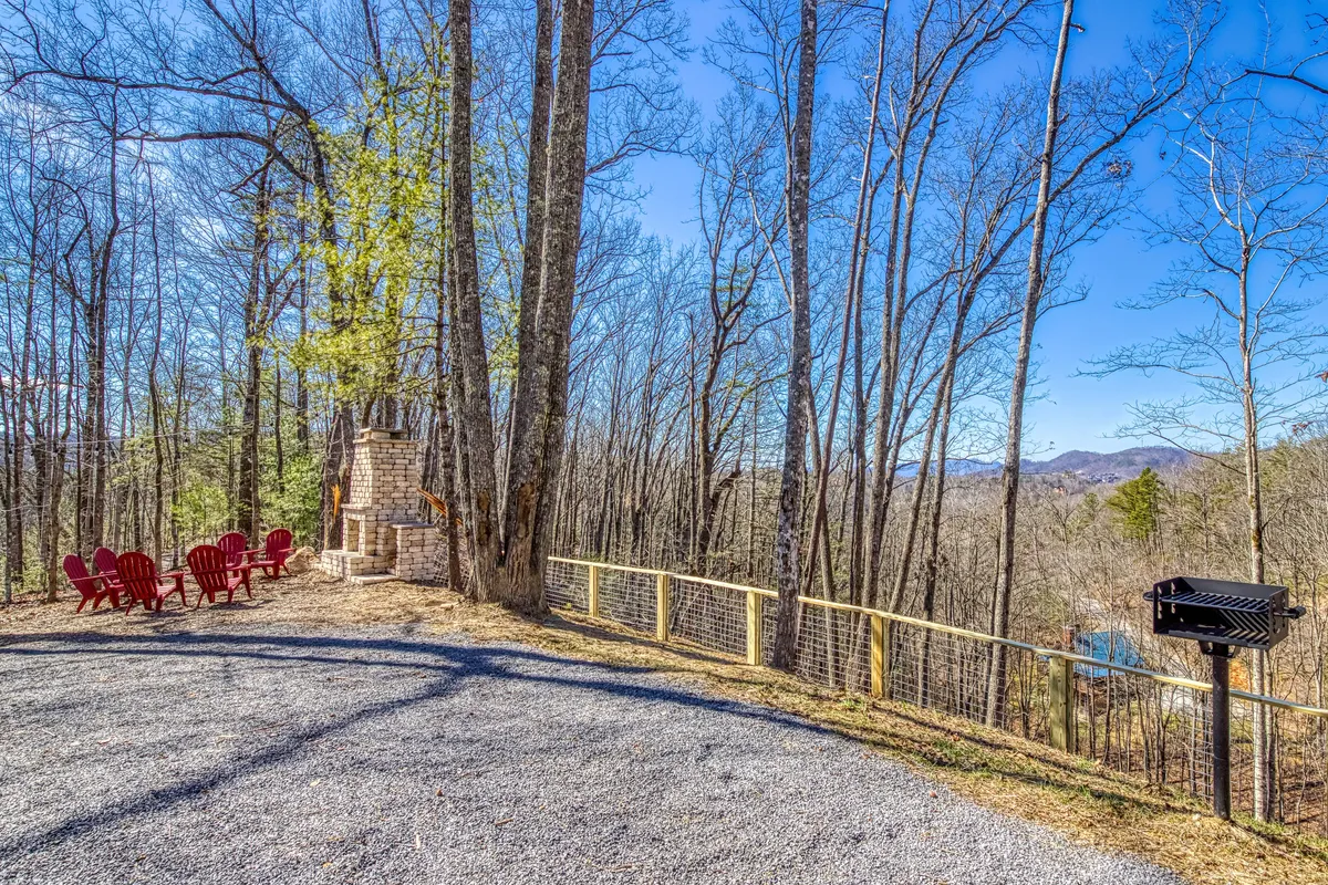 A cozy outdoor patio area featuring red Adirondack chairs around a stone fireplace, set against a backdrop of dense forest. The area is ideal for gathering, relaxing after outdoor excursions, and enjoying sunset or stargazing.