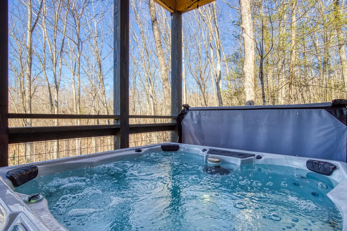 This image showcases a luxurious hot tub set on a deck surrounded by lush Smoky Mountain trees. The scene captures the tranquility and privacy of the outdoor space, inviting relaxation under the open sky. The setting suggests opportunities for stargazing or enjoying a morning coffee immersed in nature.