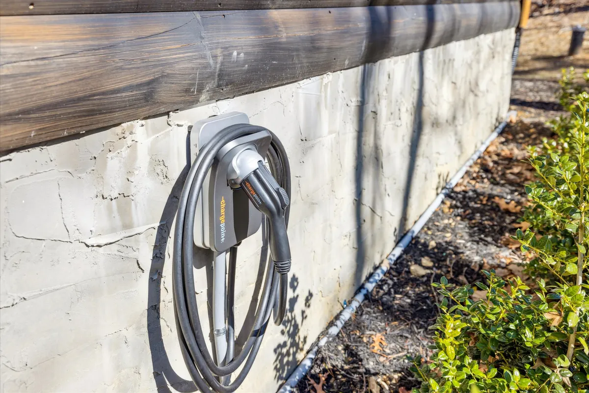 An electric vehicle charging station is framed by a textured wall and green shrubbery, highlighting sustainability in a natural environment. The scene subtly integrates eco-friendly amenities with outdoor living.