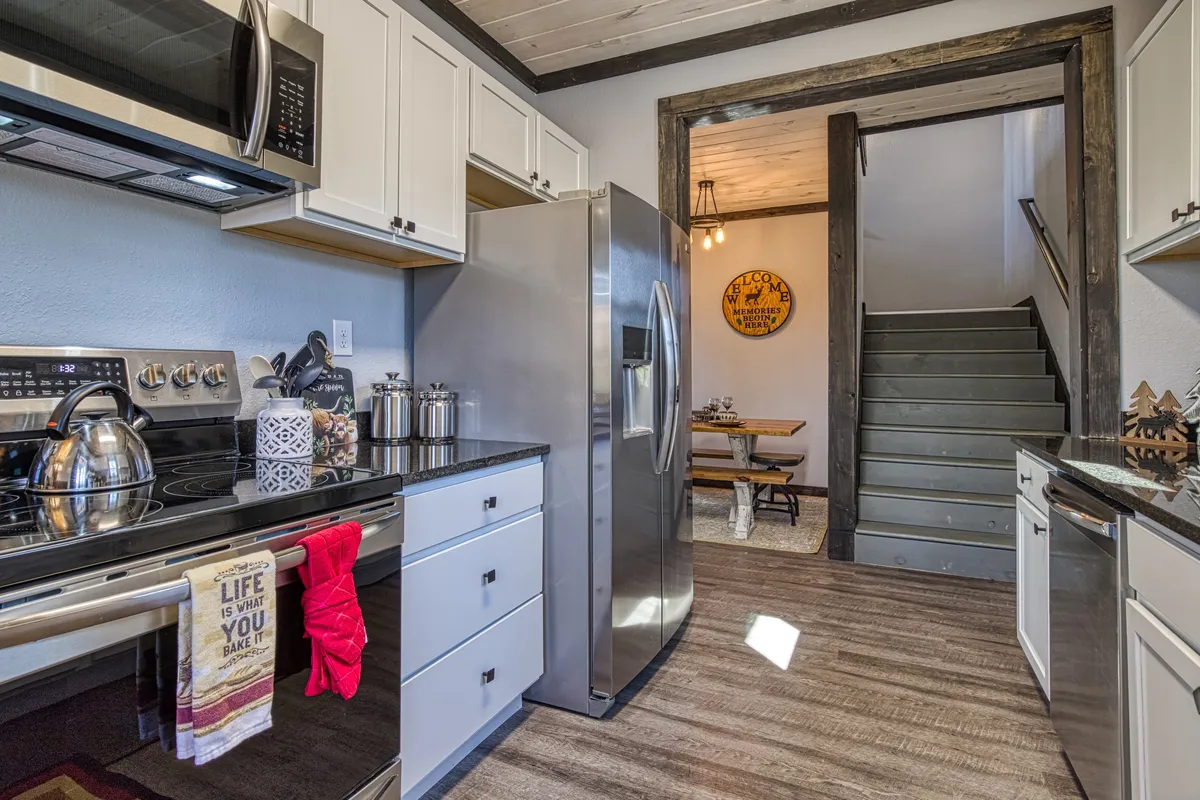 A view of the kitchen and dining area featuring stainless steel appliances, granite countertops, and a rustic wooden dining space. The setup exudes warmth and functionality, perfect for both cooking and entertaining.