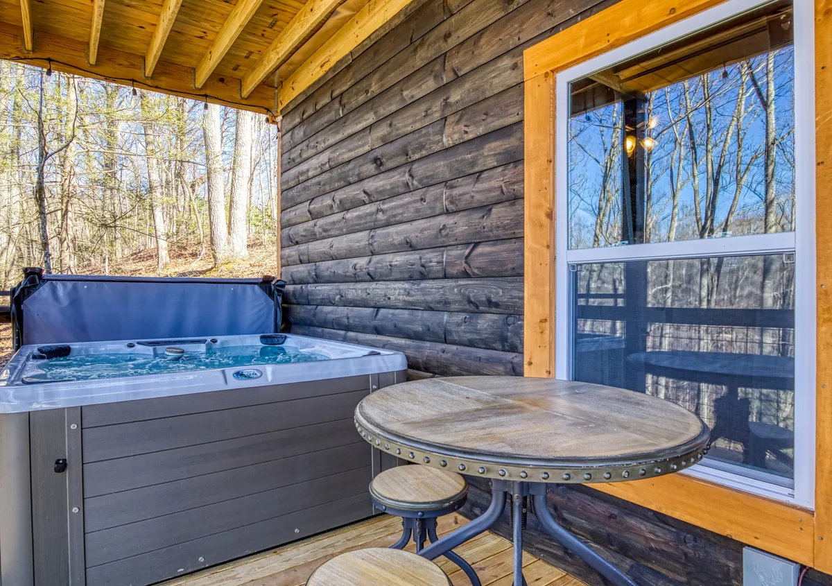 A tranquil exterior space featuring a private hot tub, wooden table, and surrounding trees. The scene radiates privacy and relaxation, with natural elements close at hand and no visible neighbors for optimal seclusion.