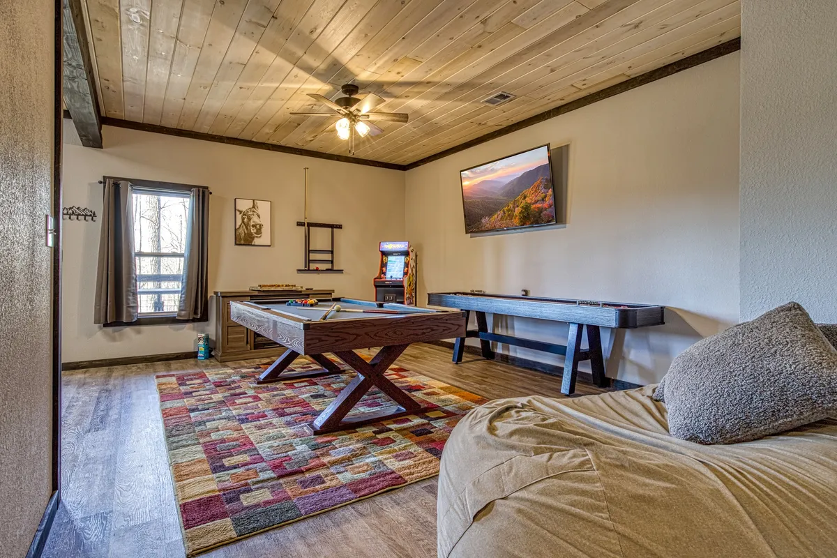 This image features a vibrant entertainment space with a pool table, an arcade game, a large TV, a colorful area rug, and comfortable seating. The arrangement invites guests to play, watch movies, or relax in a fun, welcoming environment.