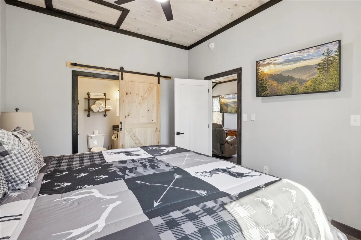 A cozy bedroom with a patterned quilt on the bed, a rustic barn door, soft wall-mounted artwork, and ambient lighting. The inviting setting invites guests to enjoy a peaceful retreat and quiet moments of relaxation.