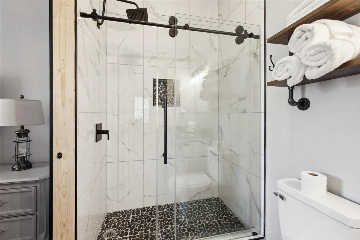 A contemporary bathroom with a glass shower enclosure, sleek black fixtures, and a pebble stone floor. The modern aesthetic and spa-like ambiance encourage relaxation and self-care, while the thoughtful design elements exude luxury and freshness.